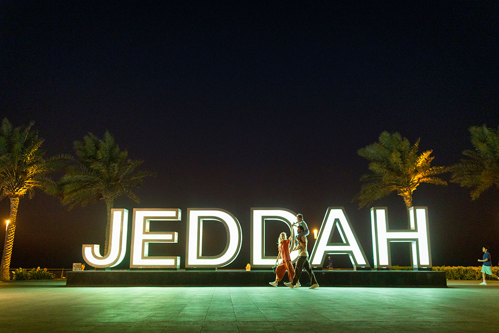 Family walking by a Jeddah sign in the night